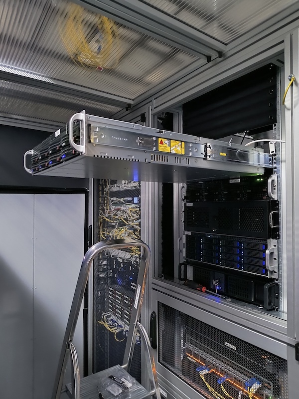 Ein Server wird mithilfe von Auszugsschienen in ein Rack im Rechenzentrum eingebaut, davor steht eine Leiter. Ein Server wird mithilfe von Auszugsschienen in ein Rack im Rechenzentrum eingebaut, davor steht eine Leiter.